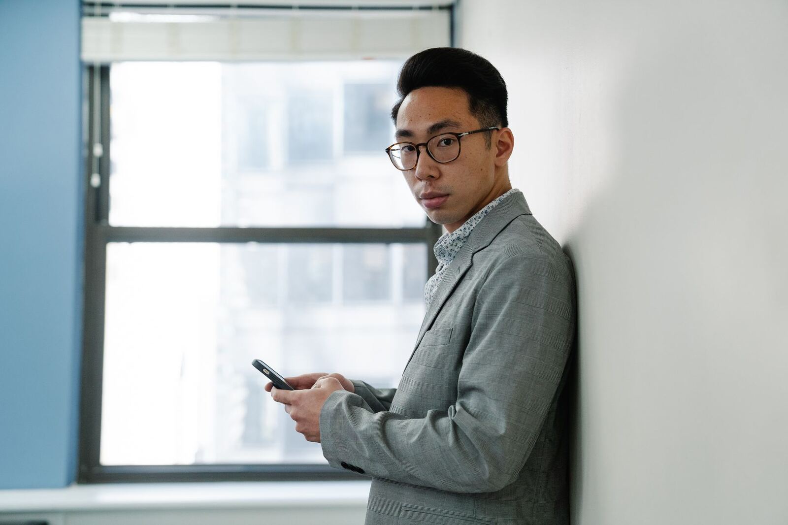 Professionally dressed man using a smartphone by a window, indoors.